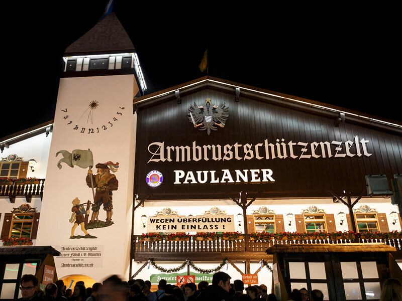 Ein Foto der erleuchteten Fassade des Armbrustschützenzelt München bei Nacht.