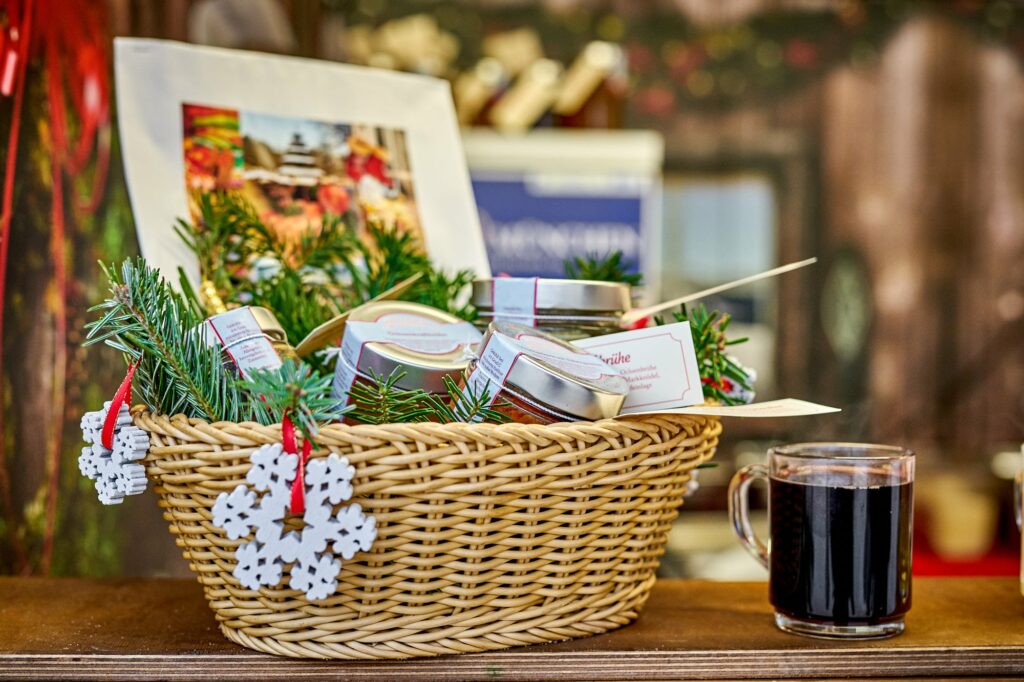 Foto von einem Körbchen gefüllt mit Tannenzweigen, Konfitüren und Weihnachtsdeko. Daneben ein Glas mit Glühwein am Weihnachtsmarktstand der Ochsenbraterei München.